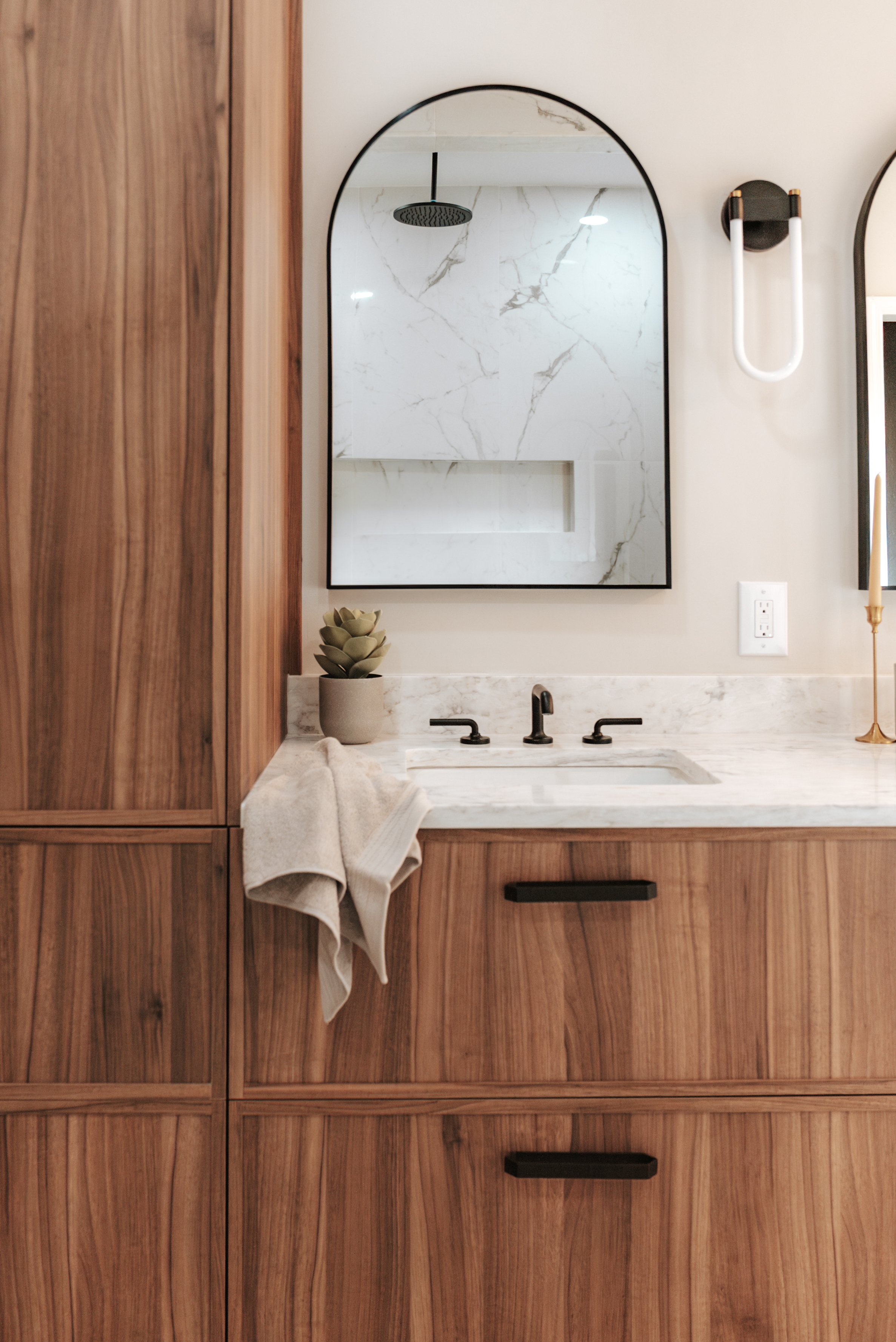 modern bathroom vanity with black matte faucet and black hardware featuring a modern bathroom light fixture and an arched mirror